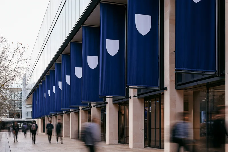 One University, Not Nine — a university building hung with a long row of deep blue banners, each carrying a single white shield