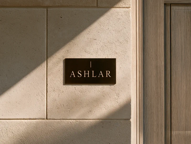 Ashlar — a bronze plaque carrying the wordmark, set into a dressed limestone wall beside an oak door